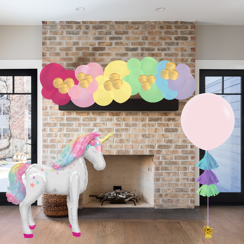 Unicorn decoration with colorful flowers and balloons in a room with a brick fireplace.